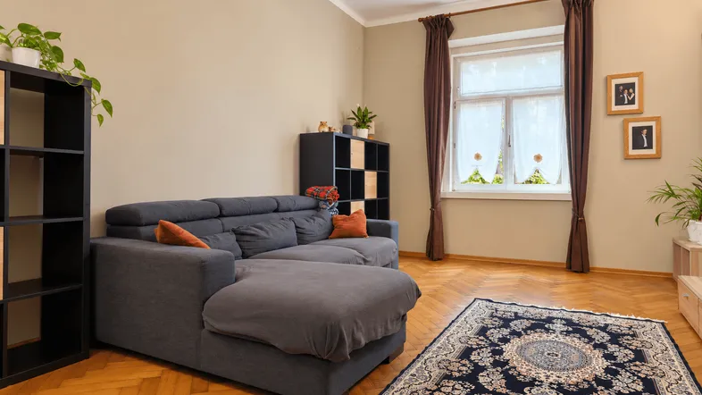 Gemütliches Wohnzimmer mit beigen Wänden, dunklem Sofa und Fischgrätparkett.
