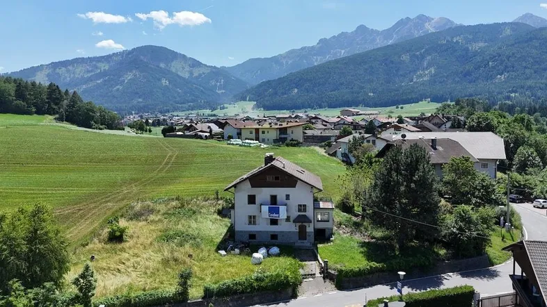 Luftaufnahme eines Hauses in ländlicher Umgebung mit weiten Feldern und Bergpanorama.