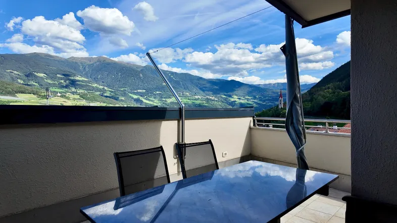 Balkon mit Tisch und Stühlen bietet einen weiten Blick auf die umliegende Berglandschaft.