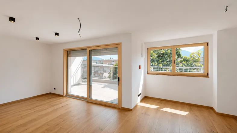 Helles Wohnzimmer mit Holzboden, weißen Wänden und Zugang zu einem sonnigen Balkon.