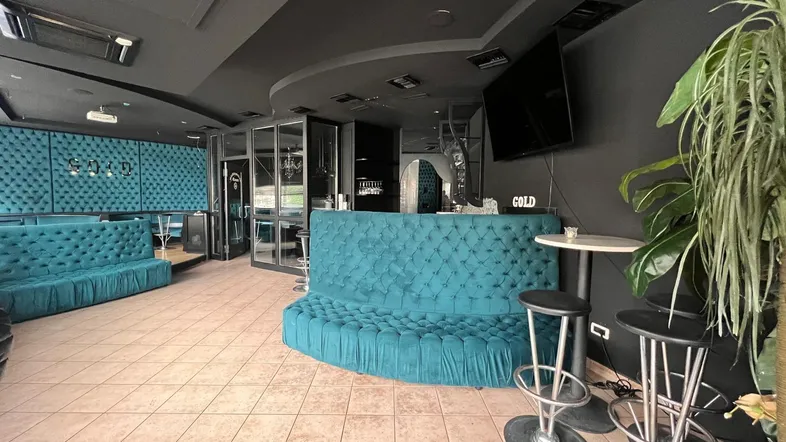 Dunkler Lounge-Bereich mit türkisfarbenen Polstermöbeln, einer Bar und Fliesenboden in modernem Design.