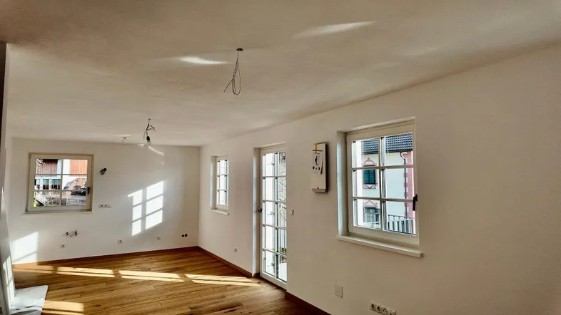 Helles, leeres Zimmer mit Holzboden und mehreren Fenstern, bereit für die Einrichtung.