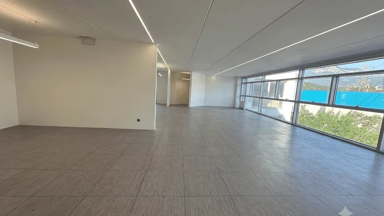 Geräumiger, leerer Büroraum mit modernen Deckenleuchten und großen Fenstern mit Bergblick.