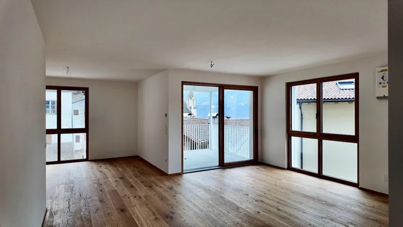 Helles Wohnzimmer mit Holzboden, großen Fenstern und Zugang zu einem Balkon mit Bergblick.