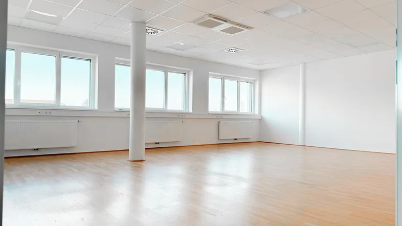 Heller, leerer Büroraum mit großen Fenstern, Säule und hellem Holzfußboden, ideal für flexible Gestaltung.
