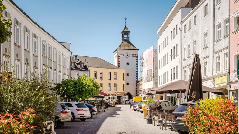 Historische Gebäude und ein Uhrturm prägen das Stadtbild dieser belebten Straße mit Cafés und Geschäften.