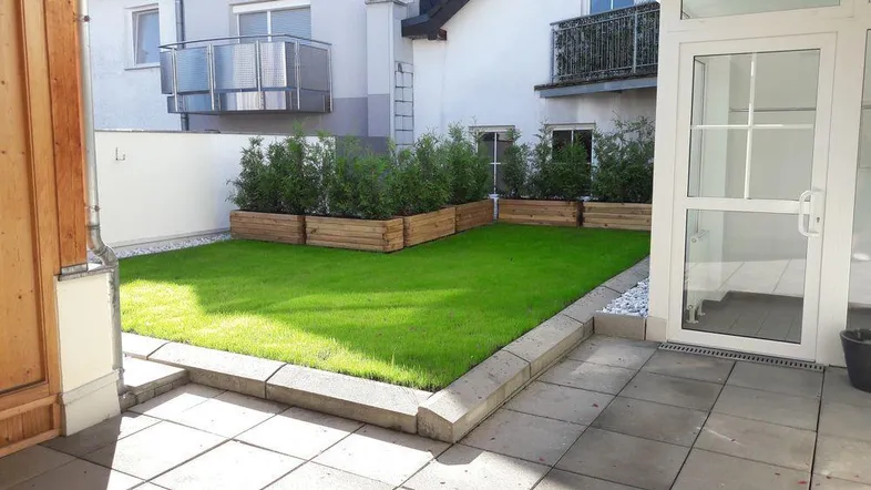 Gepflegter Gartenbereich mit Rasenfläche und Holzbeeten, direkt zugänglich von einer kleinen Terrasse.
