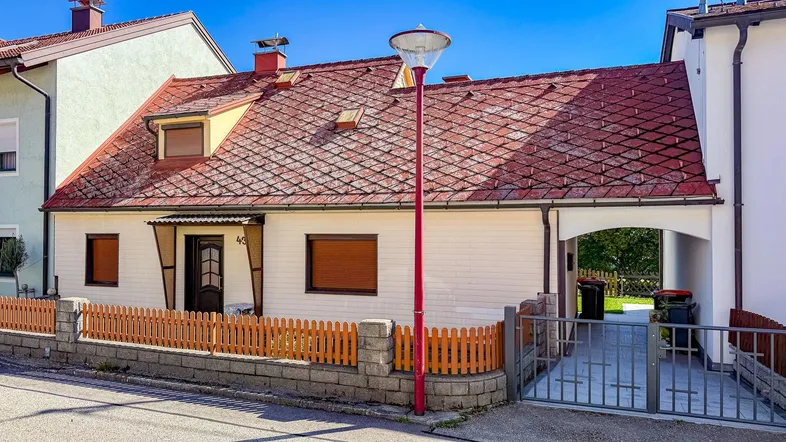 Traditionelles Einfamilienhaus mit rotem Ziegeldach, kleiner Veranda und Vorgarten.