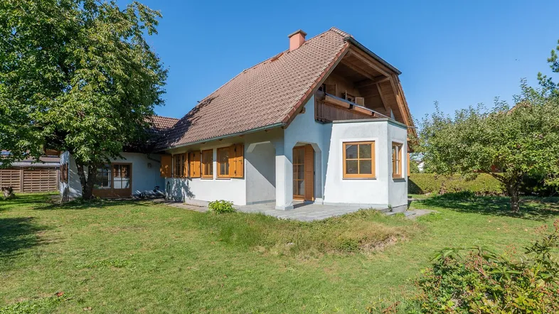 Traditionelles Einfamilienhaus mit Satteldach, Garten und kleiner Terrasse unter blauem Himmel.