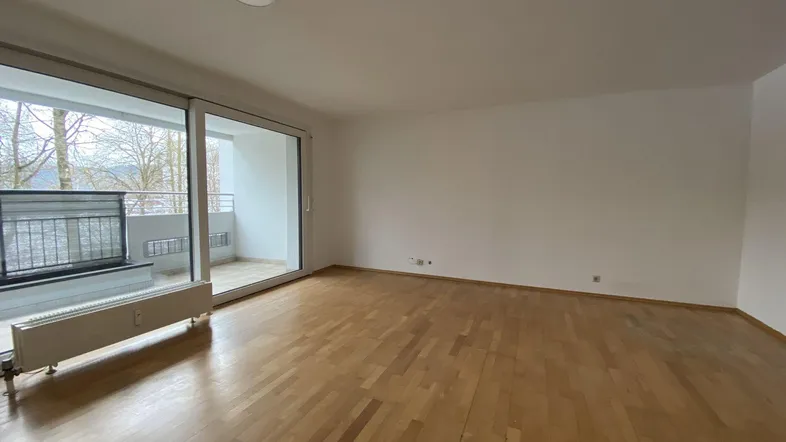 Heller, leerer Raum mit Parkettboden, weißen Wänden und großem Schiebetürzugang zum Balkon.