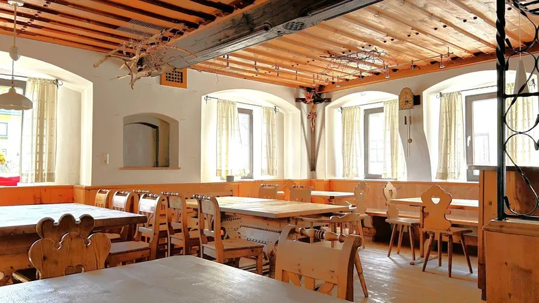 Geräumiger Speisesaal mit traditionellen Holzmöbeln, Holzbalkendecke und mehreren Fenstern.