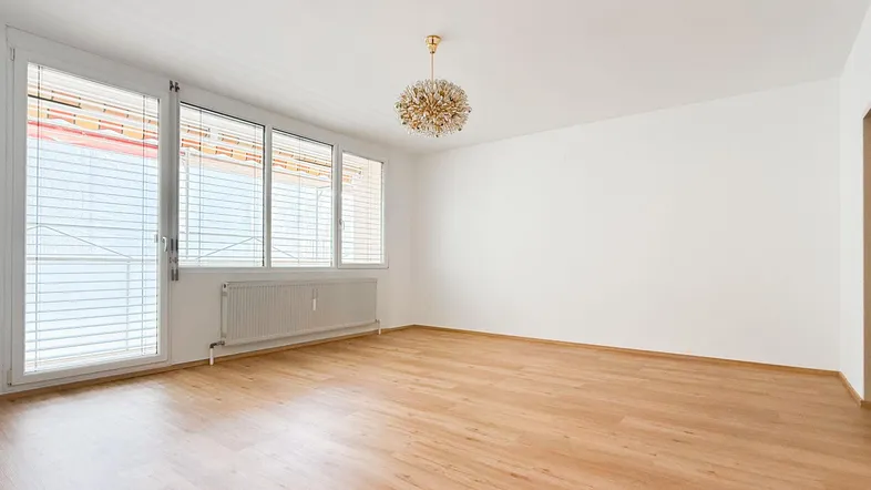 Geräumiges Wohnzimmer mit hellem Parkettboden, großen Fenstern und einem eleganten Kronleuchter.