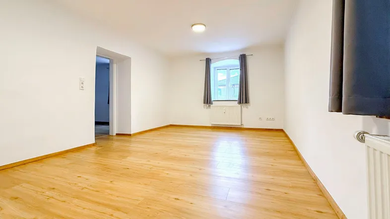 Geräumiges, leeres Zimmer mit Parkettboden und einem Fenster, das viel natürliches Licht bietet.