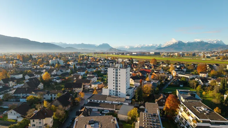 Panoramablick aus der Vogelperspektive über eine Stadt mit Bergen im Hintergrund.
