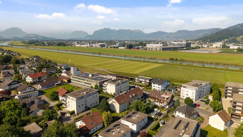 Weitläufige Luftaufnahme einer Stadt mit Wohngebäuden, Feldern und Bergen im Hintergrund.