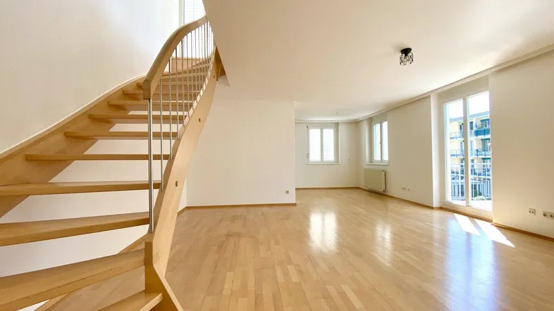 Helles und geräumiges Wohnzimmer mit eleganten Holztreppen und großen Fenstern, die viel Tageslicht hereinlassen.