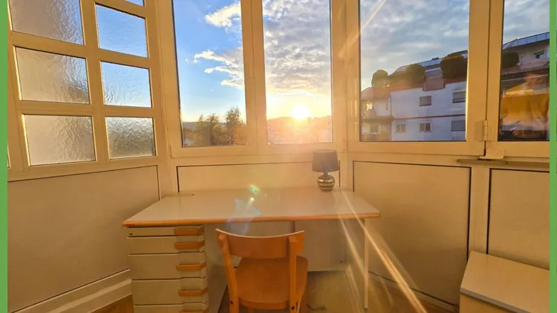 Helles Büro mit Schreibtisch und Stuhl, bietet einen weiten Blick in die Ferne bei Sonnenuntergang.