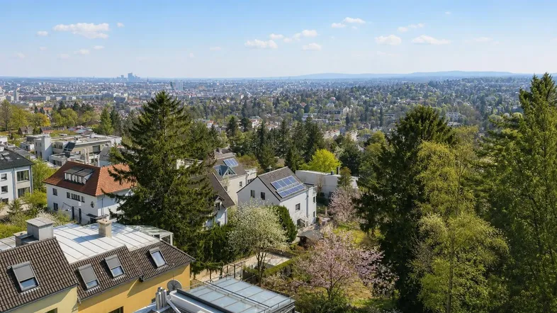 Weitläufiger Blick über eine grüne Vorstadtlandschaft mit Häusern und der Skyline in der Ferne.