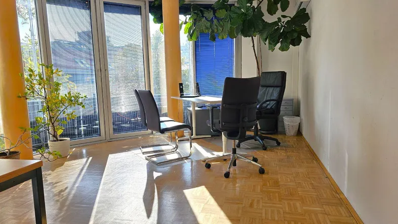 Helles Büro mit großen Fenstern, Parkettboden und mehreren Arbeitsplätzen, ideal für produktives Arbeiten.