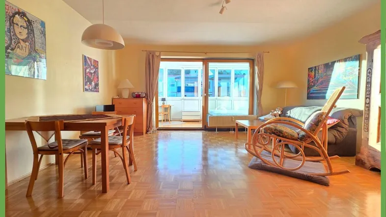 Helles Wohn- und Esszimmer mit Parkettboden und Zugang zu einem verglasten Balkon.