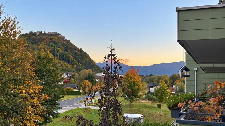 Panoramablick auf die umliegende Landschaft mit Bergen und einer Burgruine auf dem Hügel bei Sonnenuntergang.