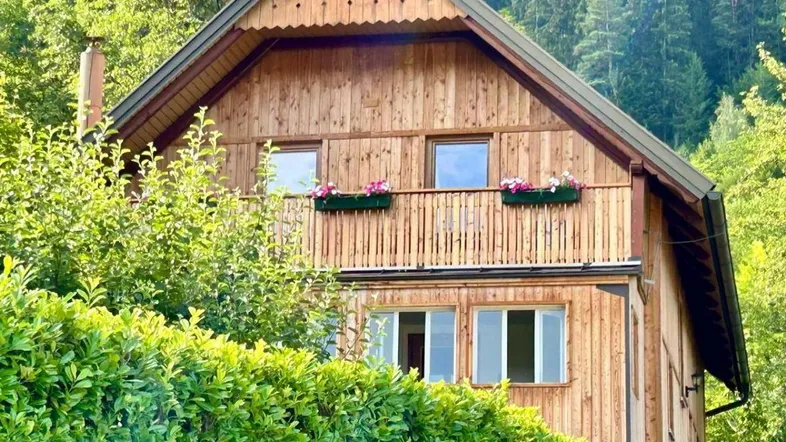 Rustikales Holzhaus in den Bergen mit grüner Umgebung und gepflegter Hecke.