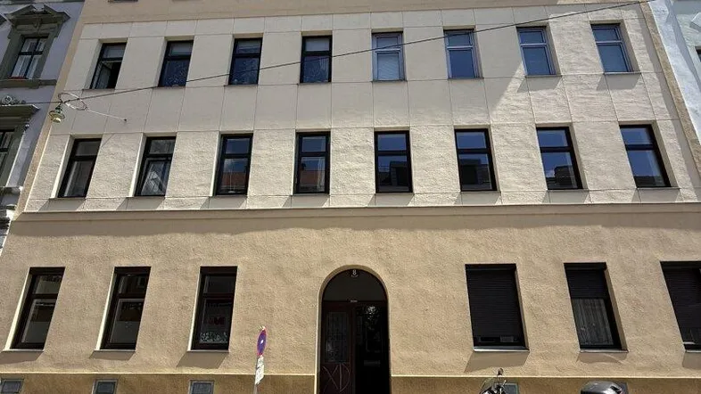 Fassade eines Altbaus mit mehreren Stockwerken und Fenstern an einem sonnigen Tag.