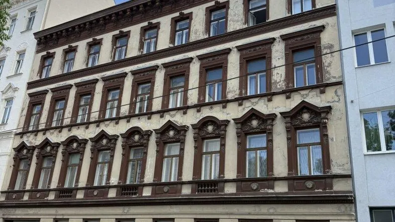 Historisches Mehrfamilienhaus mit reich verzierter Fassade und sichtbaren Gebrauchsspuren in urbaner Umgebung.