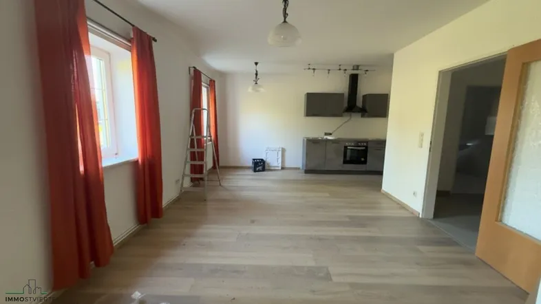 Heller offener Wohn- und Essbereich mit Laminatboden und einer Küchenzeile im Hintergrund.