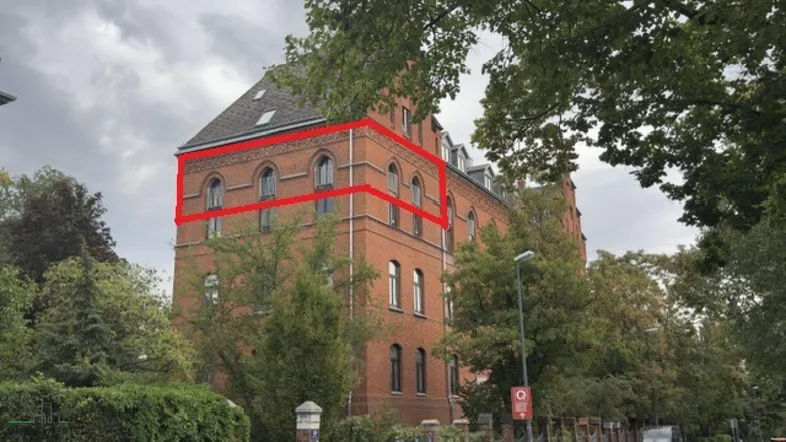 Historisches Backsteingebäude mit markanten Rundbogenfenstern und grüner Umgebung unter bewölktem Himmel.