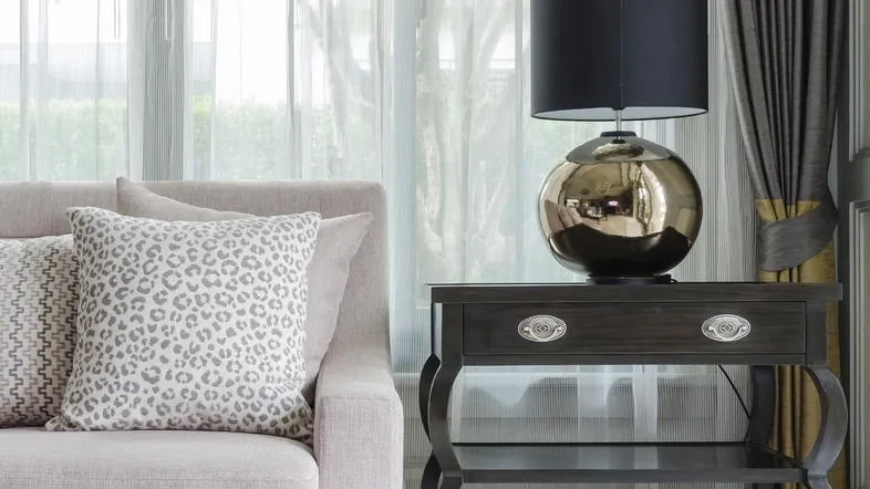 Gemütliches Wohnzimmer mit hellem Sofa, elegantem Beistelltisch und dekorativer Lampe am Fenster.