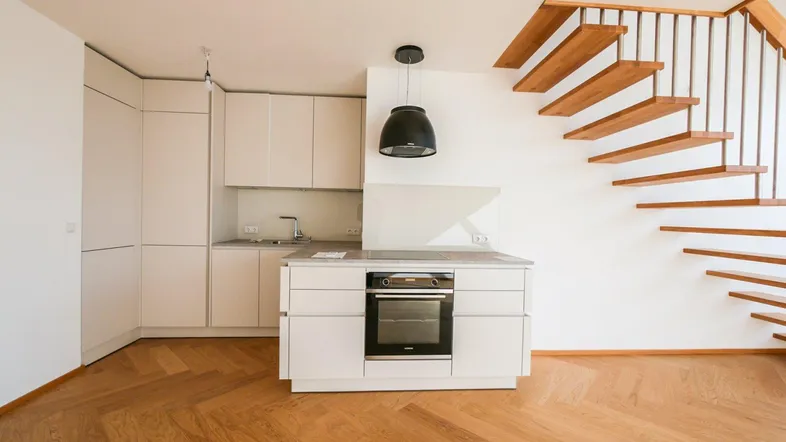 Moderne Einbauküche mit hellem Holzparkett und offener Treppe zu einer oberen Ebene.