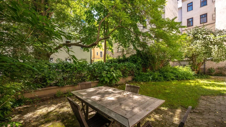 Ruhiger Innenhofgarten mit Holztisch und Stühlen, umgeben von üppigem Grün und Bäumen.