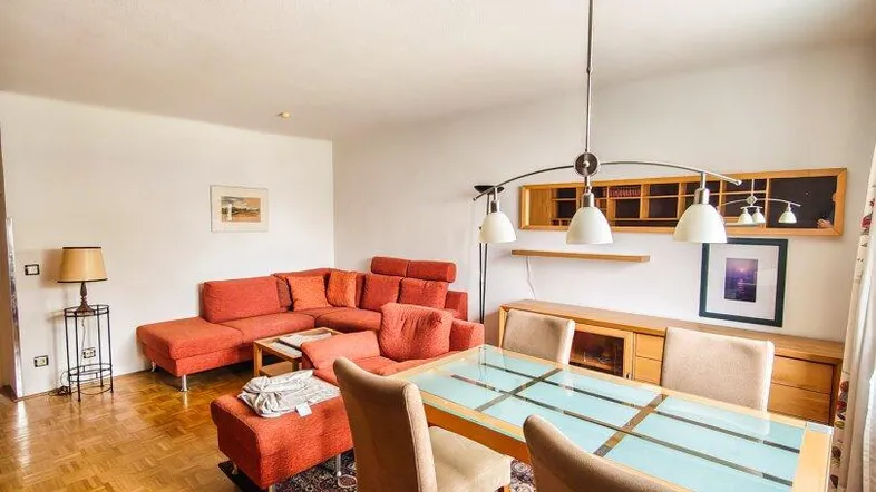 Geräumiger Wohn-Essbereich mit Parkettboden, rotem Sofa und Esstisch in heller Atmosphäre.