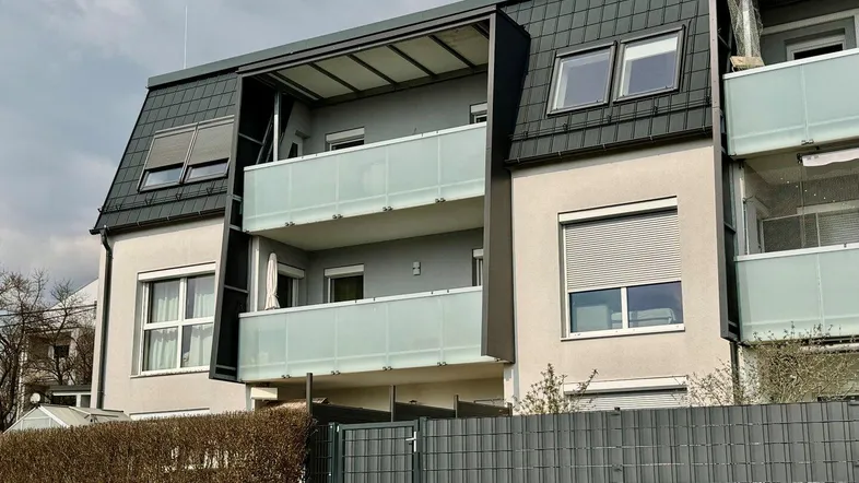 Moderne Gebäudefassade mit Balkonen und Mansarddach in einer Wohnsiedlung.