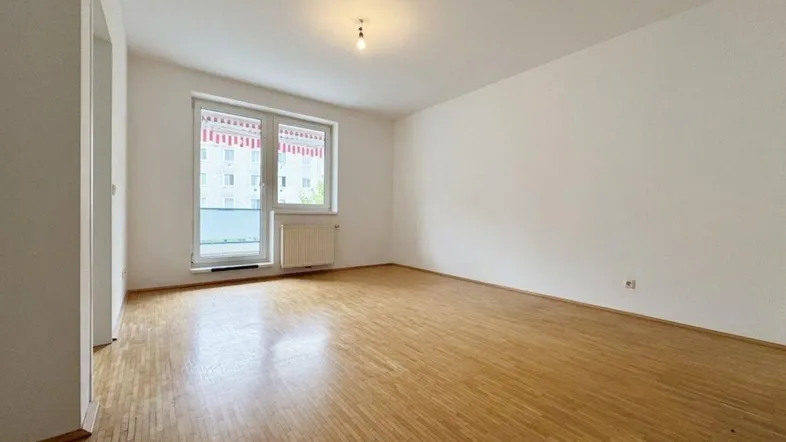 Helles, leeres Zimmer mit Parkettboden und großem Fenster mit Zugang zum Balkon.