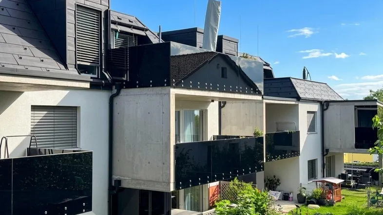 Moderne Wohnanlage mit mehreren Balkonen und Dachgauben unter blauem Himmel.