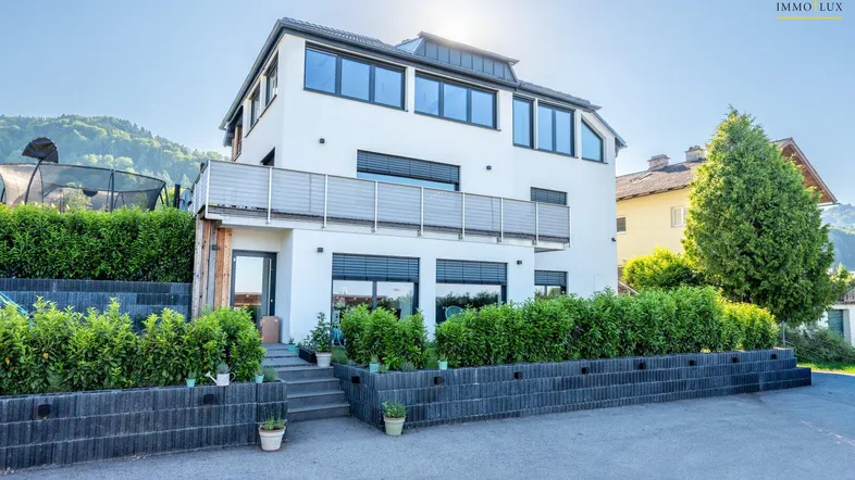 Modernes Wohnhaus mit Balkon, gepflegter Hecke und Bergblick.