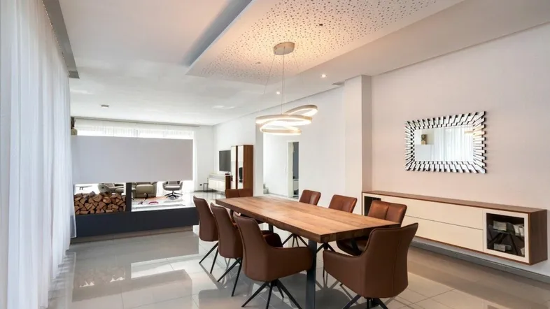 Eleganter Essbereich mit großem Holztisch, modernen Stühlen und dekorativer Deckenbeleuchtung.