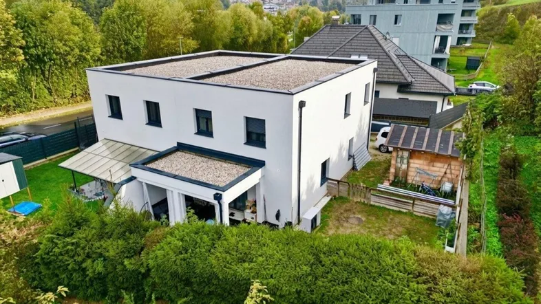 Modernes Einfamilienhaus mit Flachdach und gepflegtem Garten in grüner Umgebung.