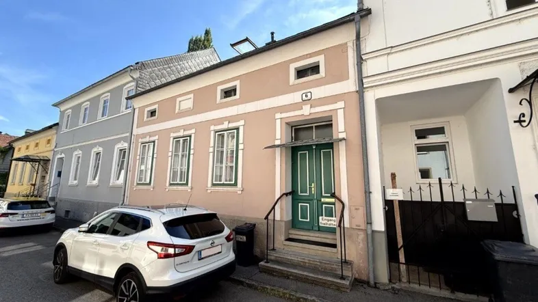 Fassade eines Wohnhauses von der Straße aus gesehen mit einem geparkten Auto davor.