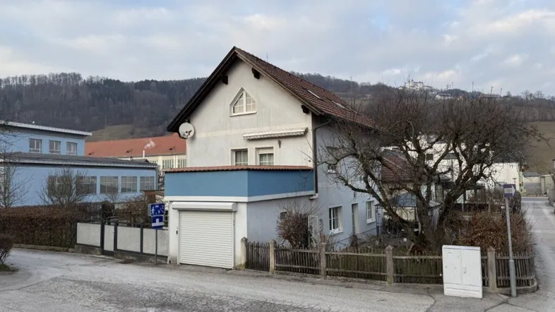 Einfamilienhaus mit Satteldach, integrierter Garage und kleinem Balkon in ländlicher Umgebung.