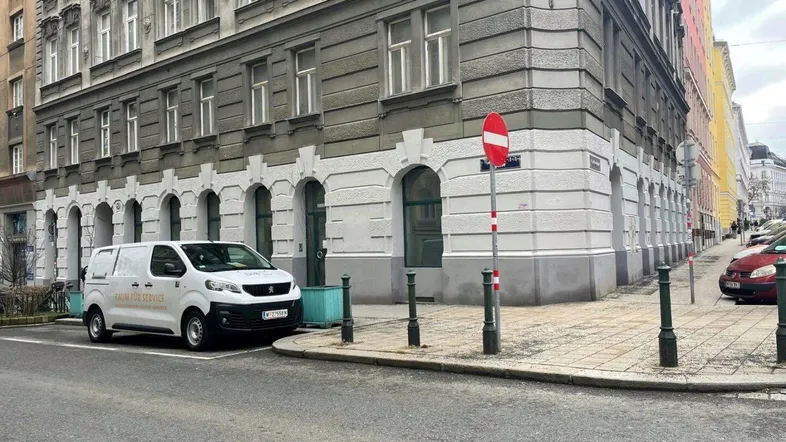 Ansicht eines historischen Gebäudes an einer Straßenecke mit einem Lieferwagen davor und umliegenden Gebäuden.