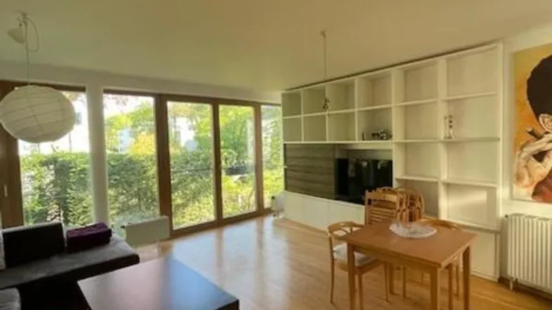 Helles Wohn- und Esszimmer mit großen Fenstern, Holzboden und Blick ins Grüne.