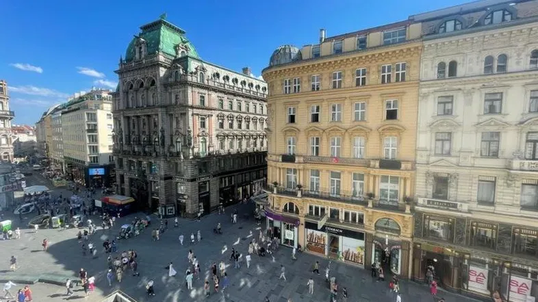 Panoramablick auf einen belebten historischen Stadtplatz mit beeindruckenden Gebäuden unter blauem Himmel.