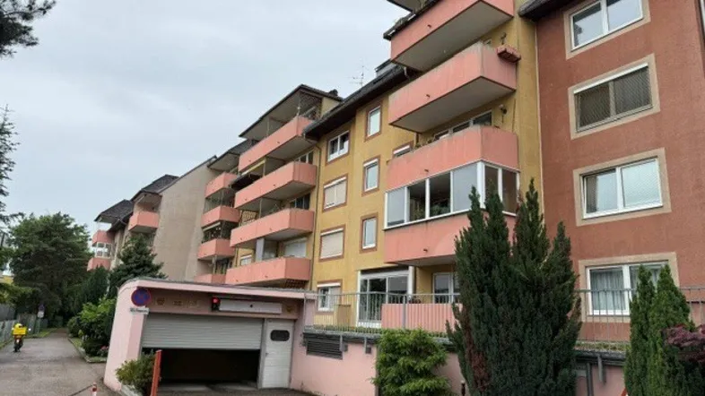 Mehrfamilienhaus mit mehreren Balkonen und Zufahrt zur Tiefgarage unter bewölktem Himmel.