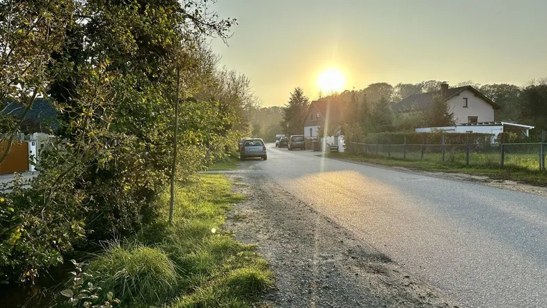 Sonnenuntergang über einer ländlichen Straße mit Häusern und Bäumen in der Ferne.