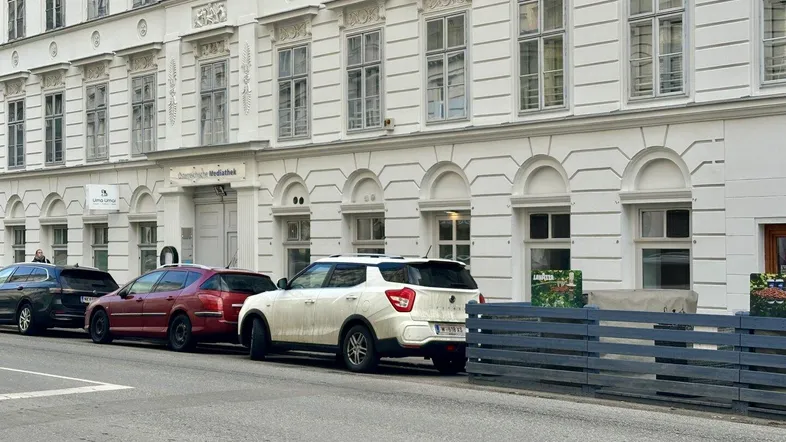 Historisches Gebäude mit klassischer Fassade und parkenden Autos auf der Straße in der Stadt.