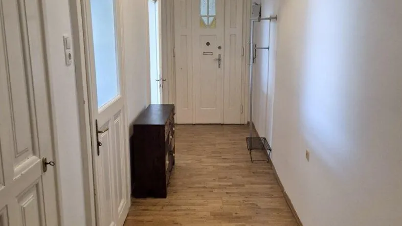 Langer, heller Flur mit Holzboden und weißen Türen, der zum Eingangsbereich führt.