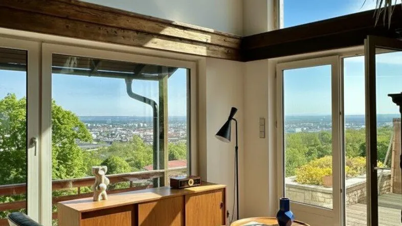Helles Wohnzimmer mit hohen Decken, Holzbalken und weitem Blick über die Stadt.